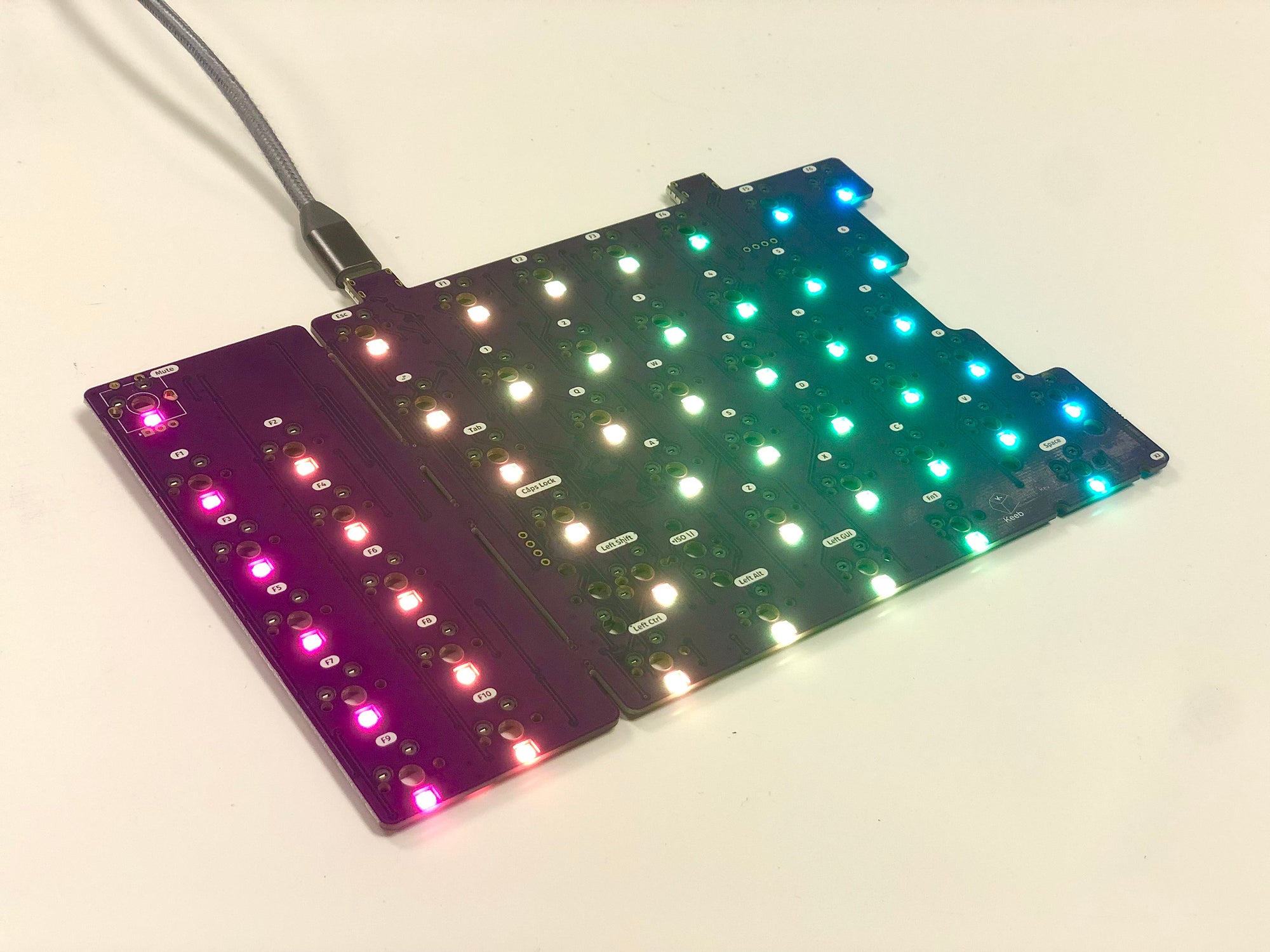Left half of a bare Sinc PCB plugged in with a columnar gradient from pink to blue on the per-key LEDs.