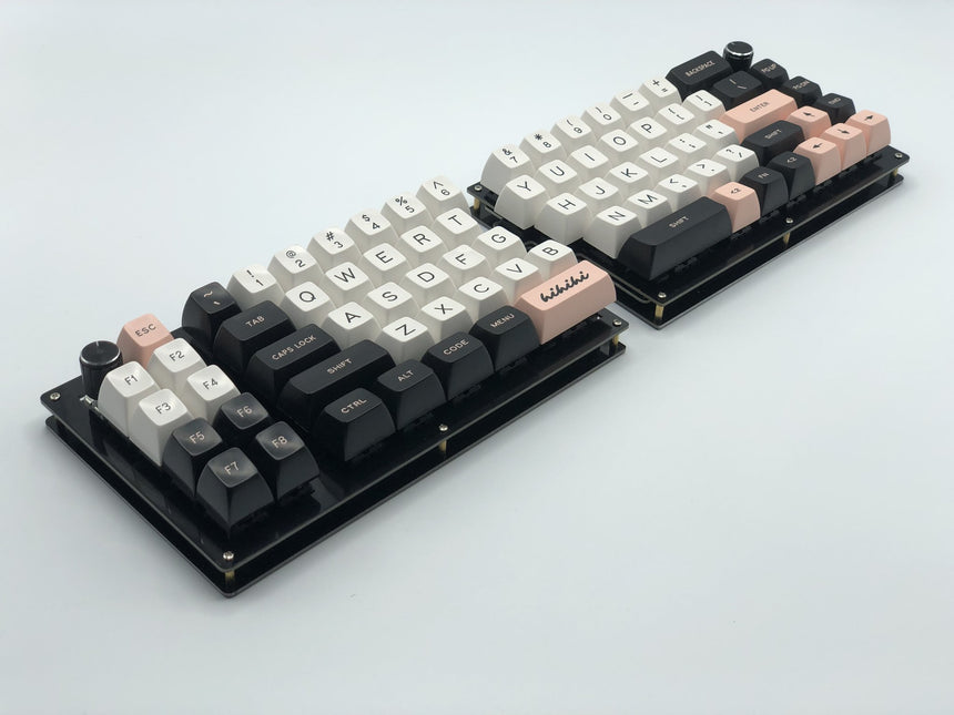 Fully built Quefrency keyboard with one rotary encoder in the outer corner of each half and black, white, and pink keycaps.